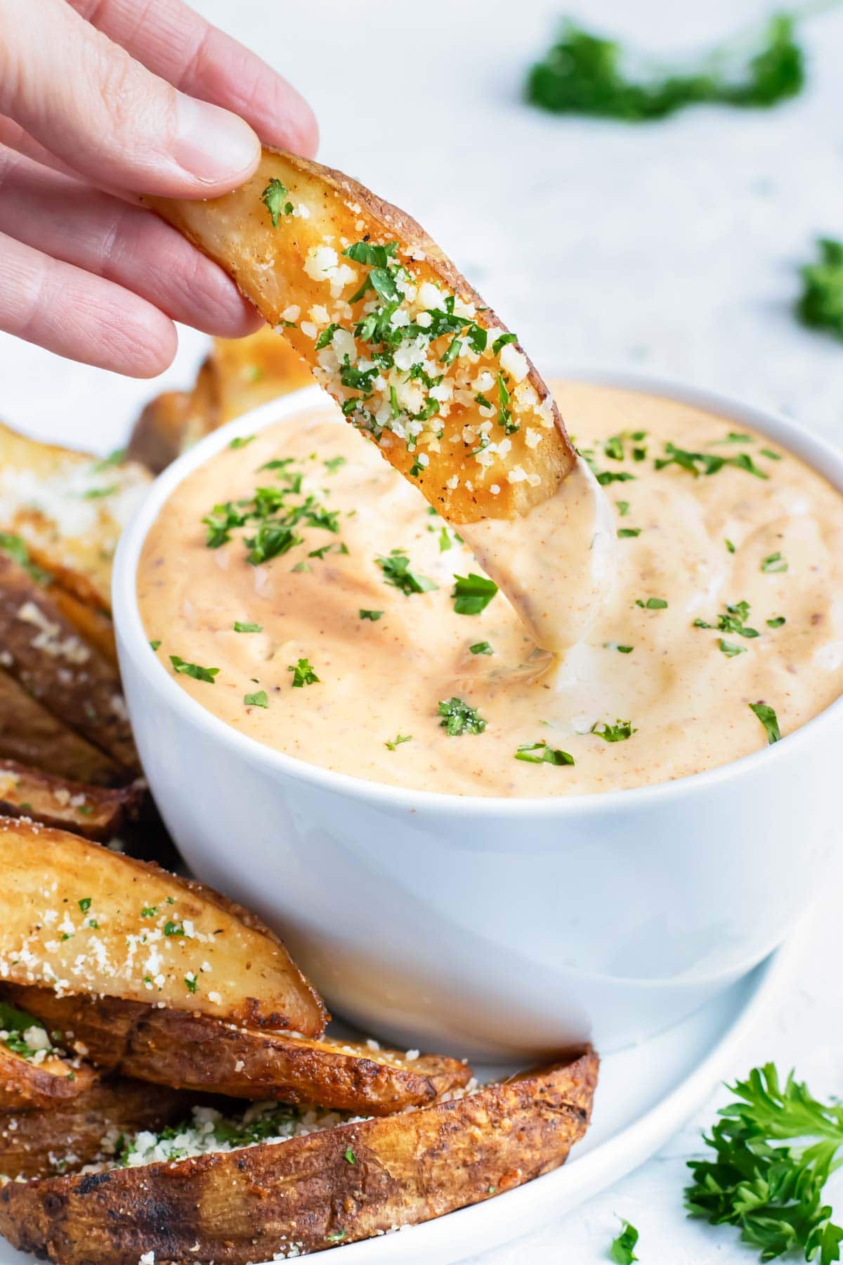 A baked potato wedge being dipped into a bowl full of Cajun remoulade sauce.