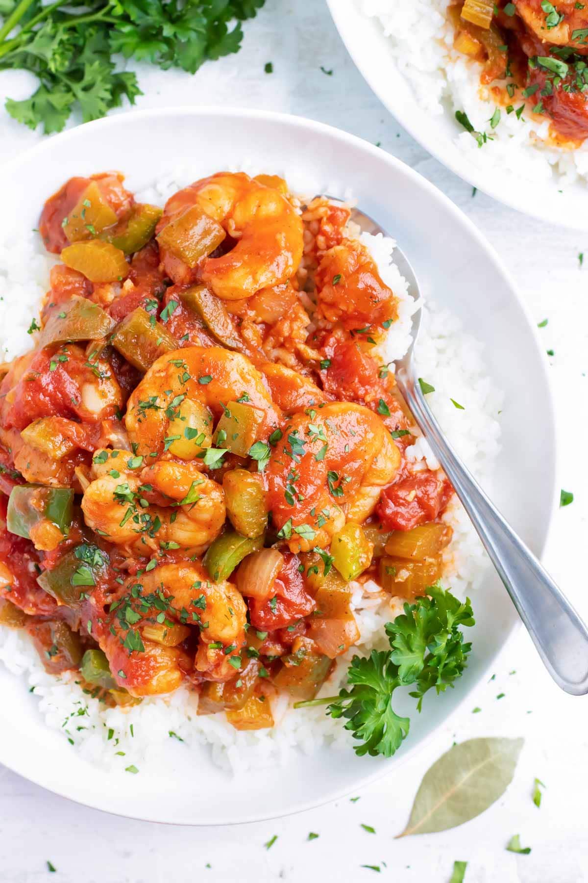The best shrimp creole recipe in a white bowl next to a bay leaf and parsley.