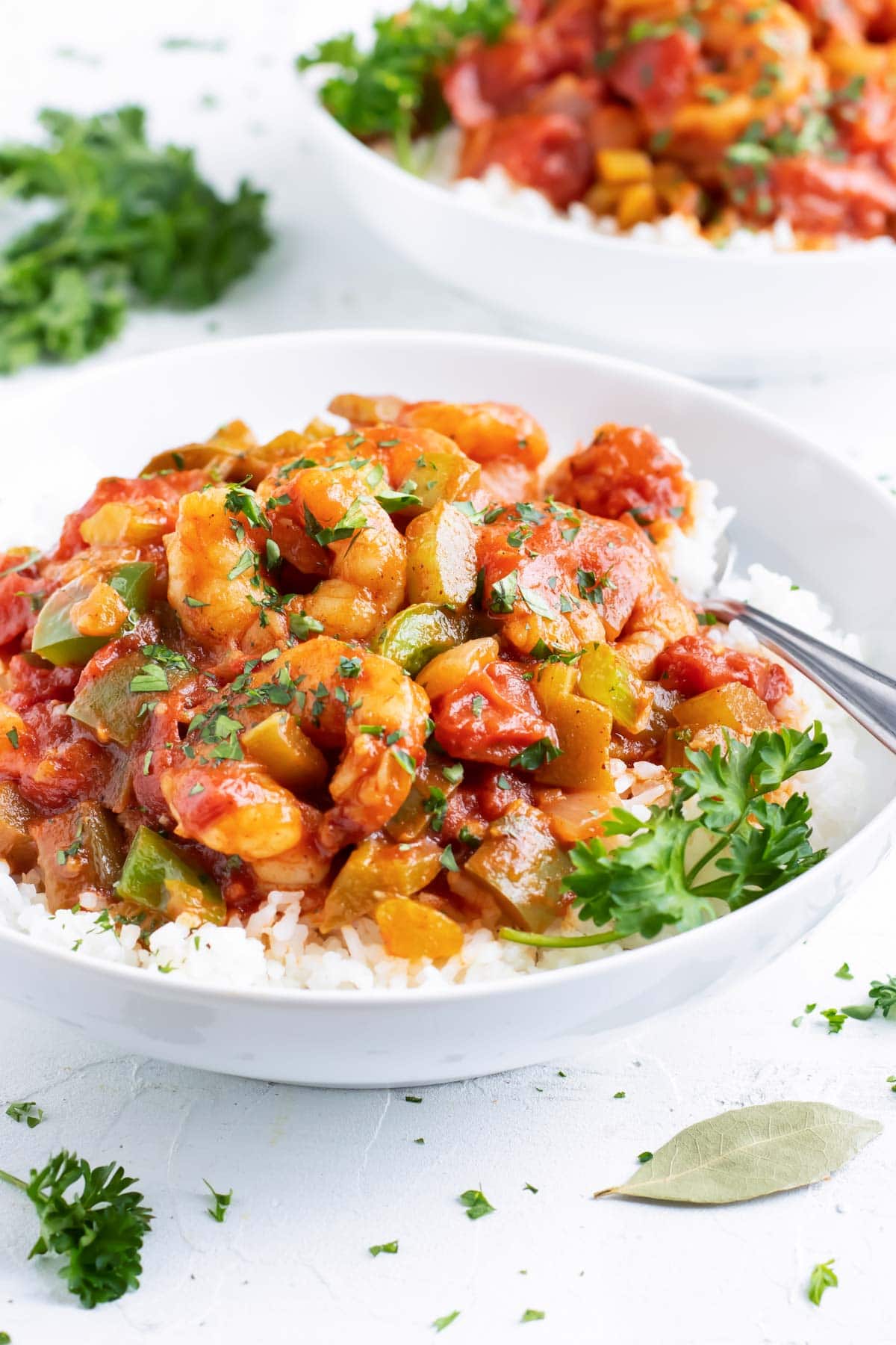 The best shrimp creole recipe in a white bowl next to a bay leaf and parsley.