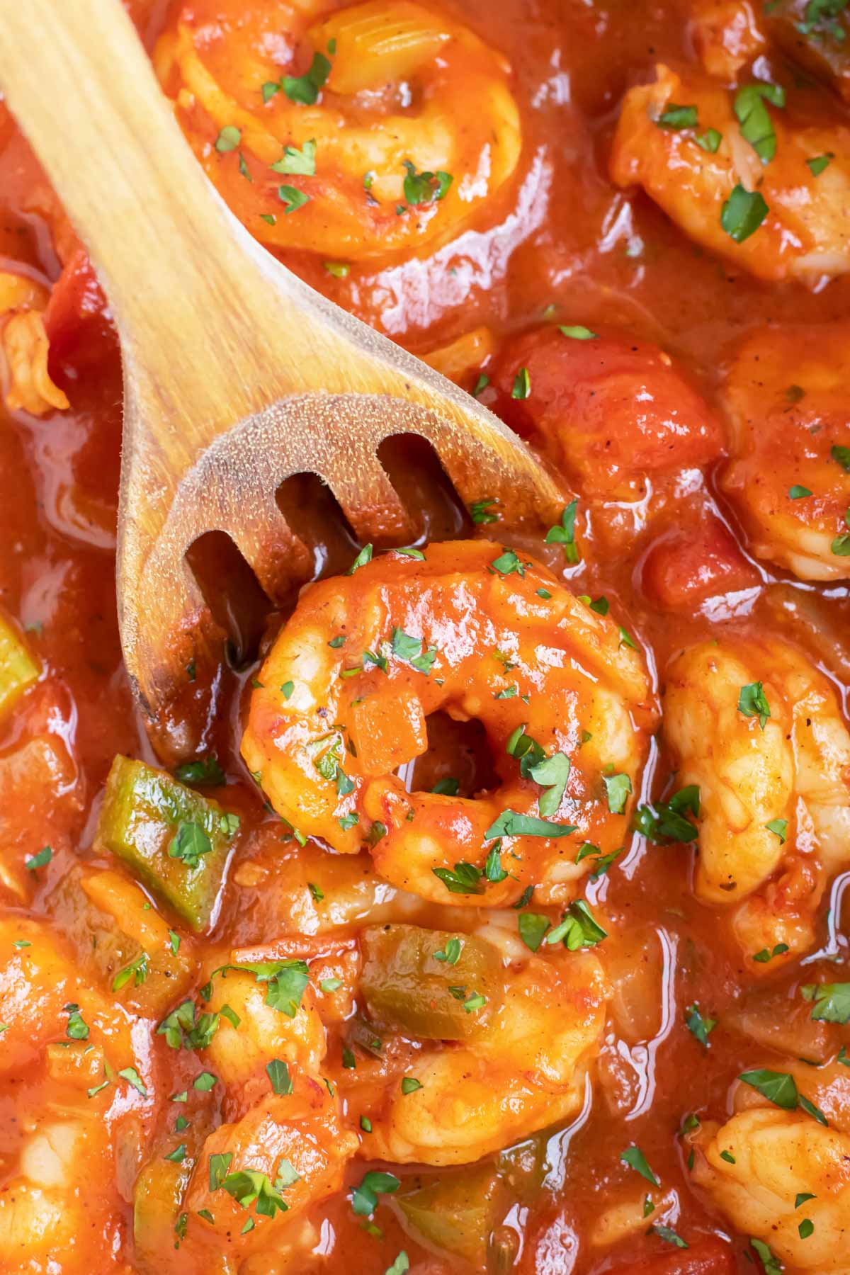 A wooden spoon scooping up a large shrimp in a Cajun tomato sauce.