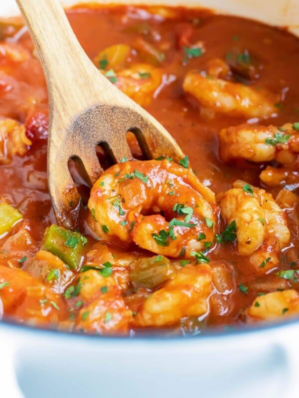 A wooden spoon scooping up a shrimp from a pot of Shrimp Creole.
