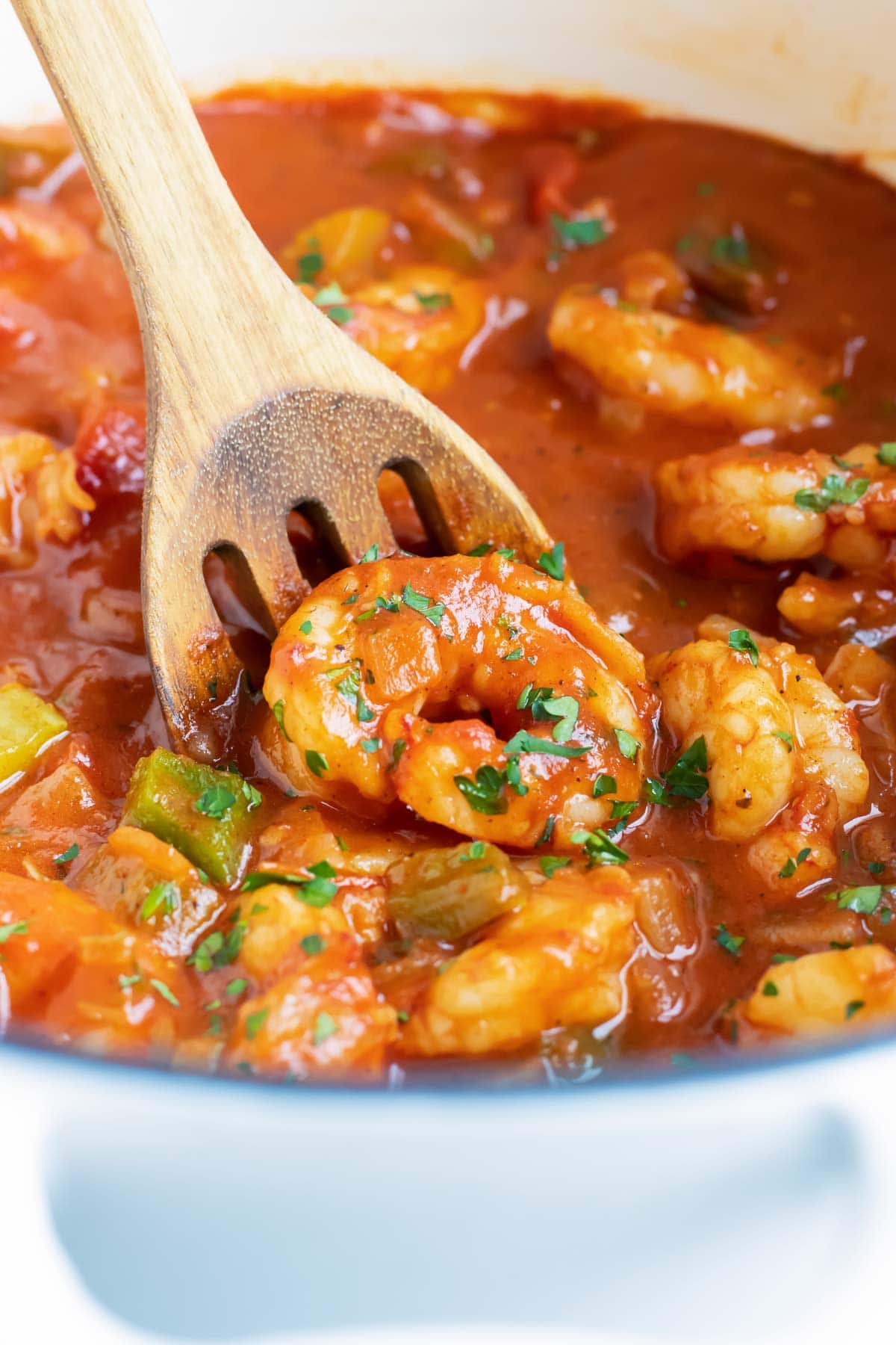 A wooden spoon scooping up a shrimp from a pot of Shrimp Creole.