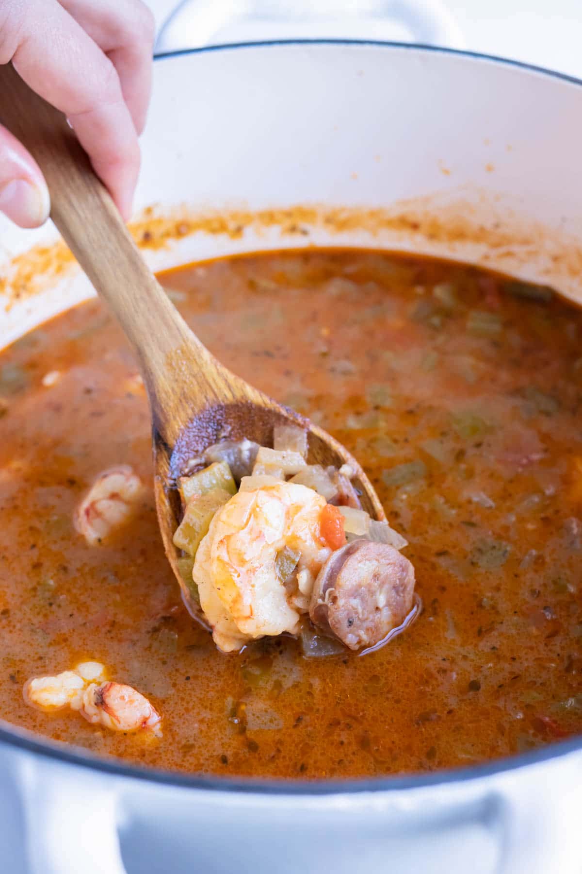 Shrimp and sausage gumbo is served from a pot with a wooden spoon.
