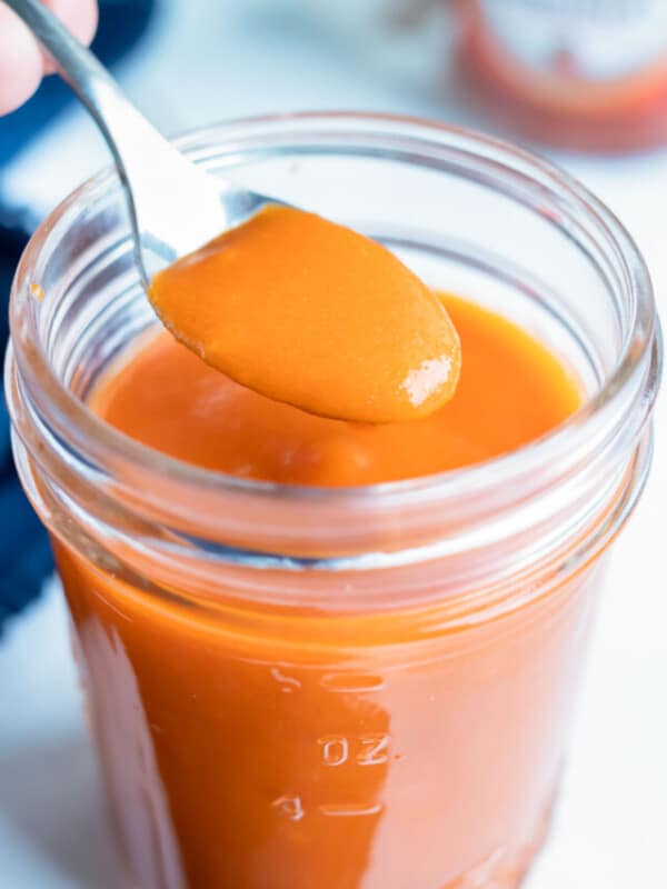 Spicy buffalo wing sauce is lifted up with a spoon before putting on wings.