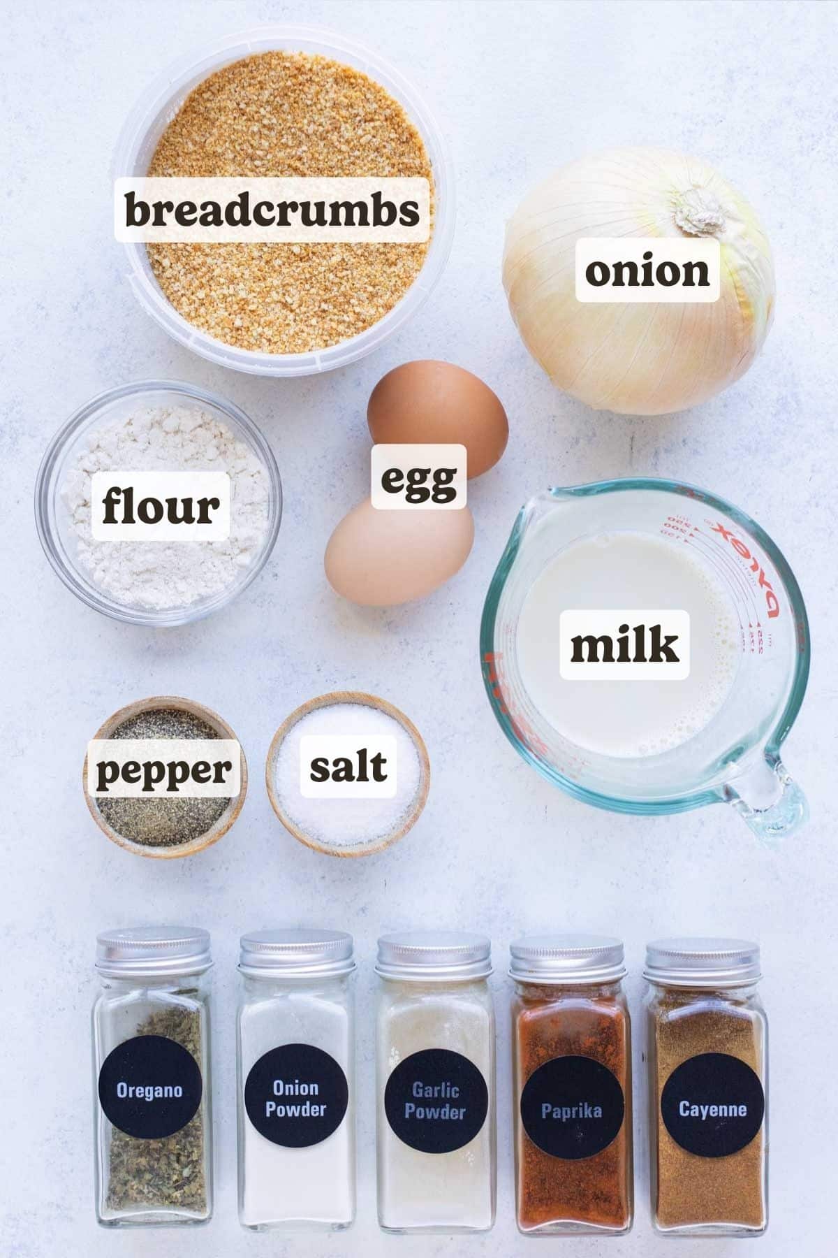 Onion, egg, milk, flour, breadcrumbs and seasonings laid out for a homemade air fryer blooming onion.