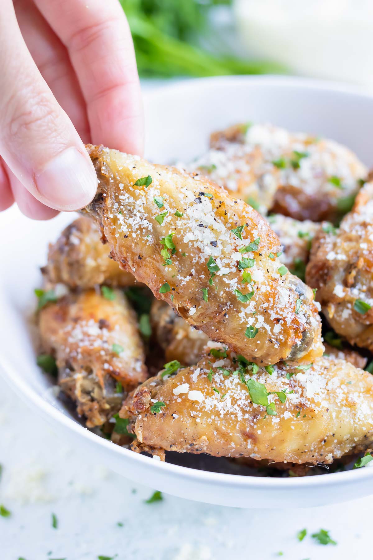 Garlic air fryer chicken wings are lifted up out of a white bowl.