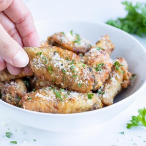 Chicken wings are lifted up by a hand for a low-carb appetizer.