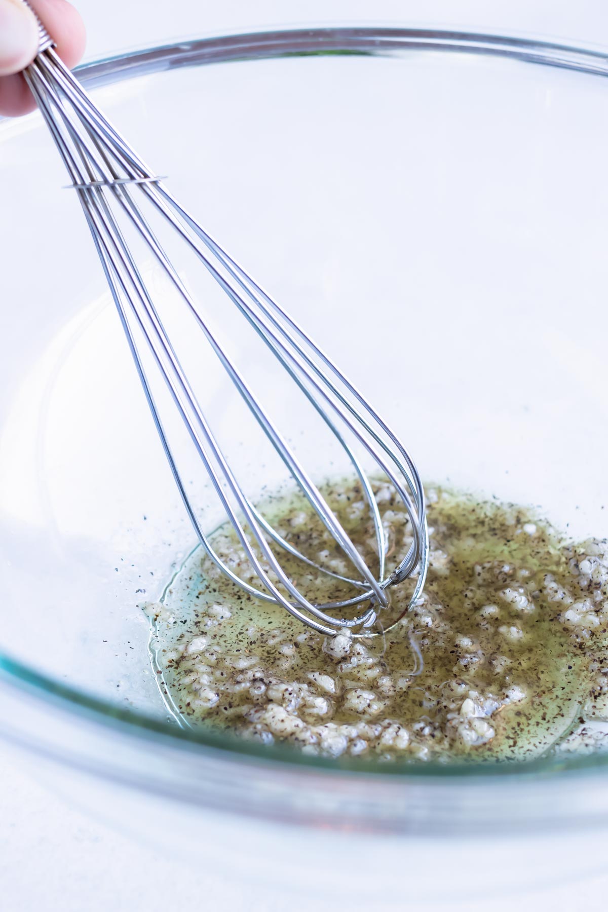 Oil, fresh garlic, and seasonings are whisked together in a glass bowl.