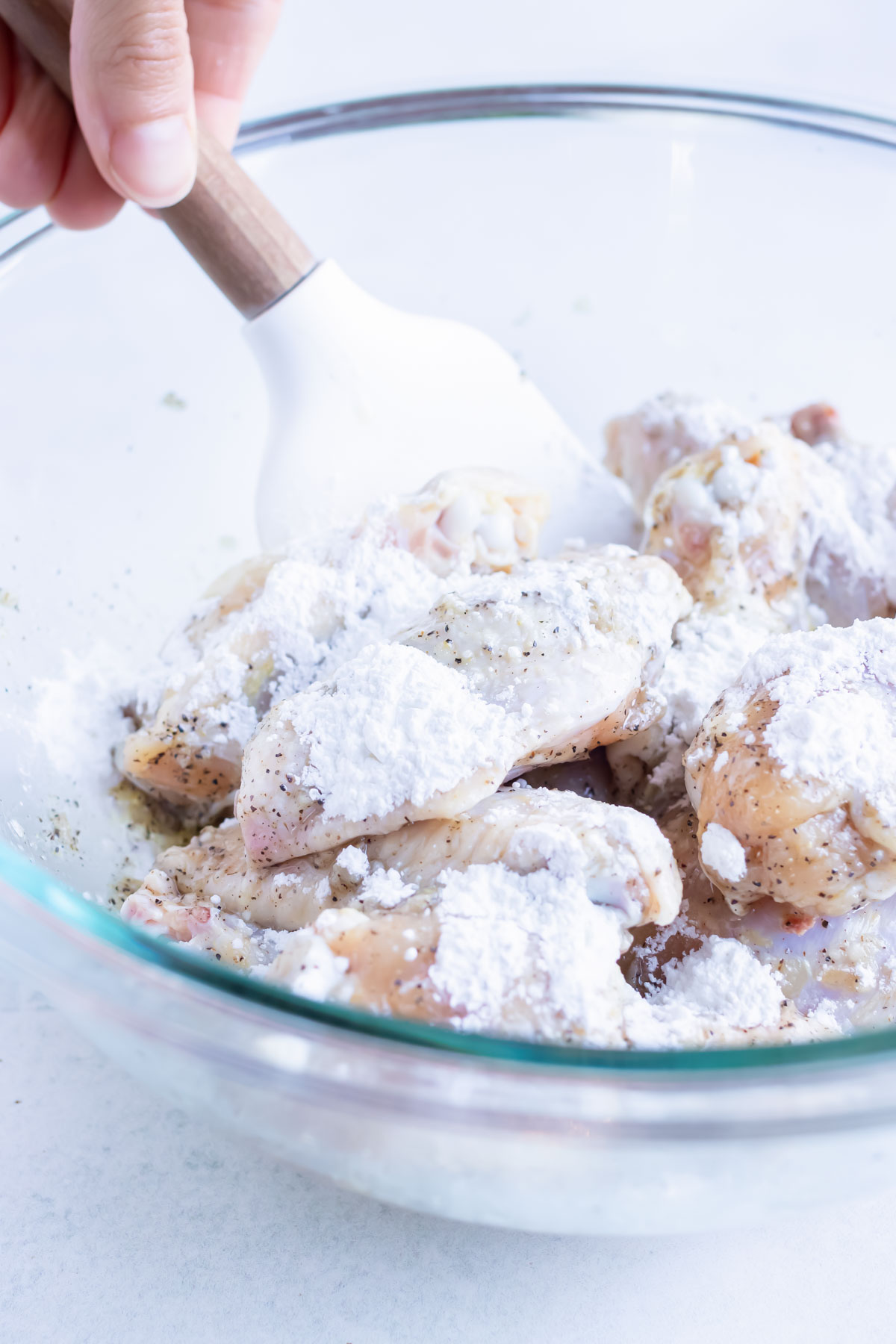 Corn starch is sprinkled on the uncooked chicken wings before air frying.