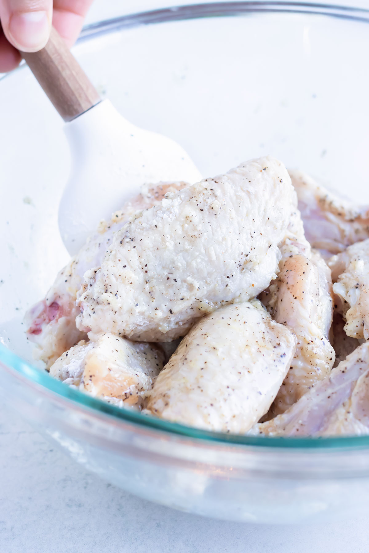 Raw chicken wings are coated with corn starch in a glass bowl.