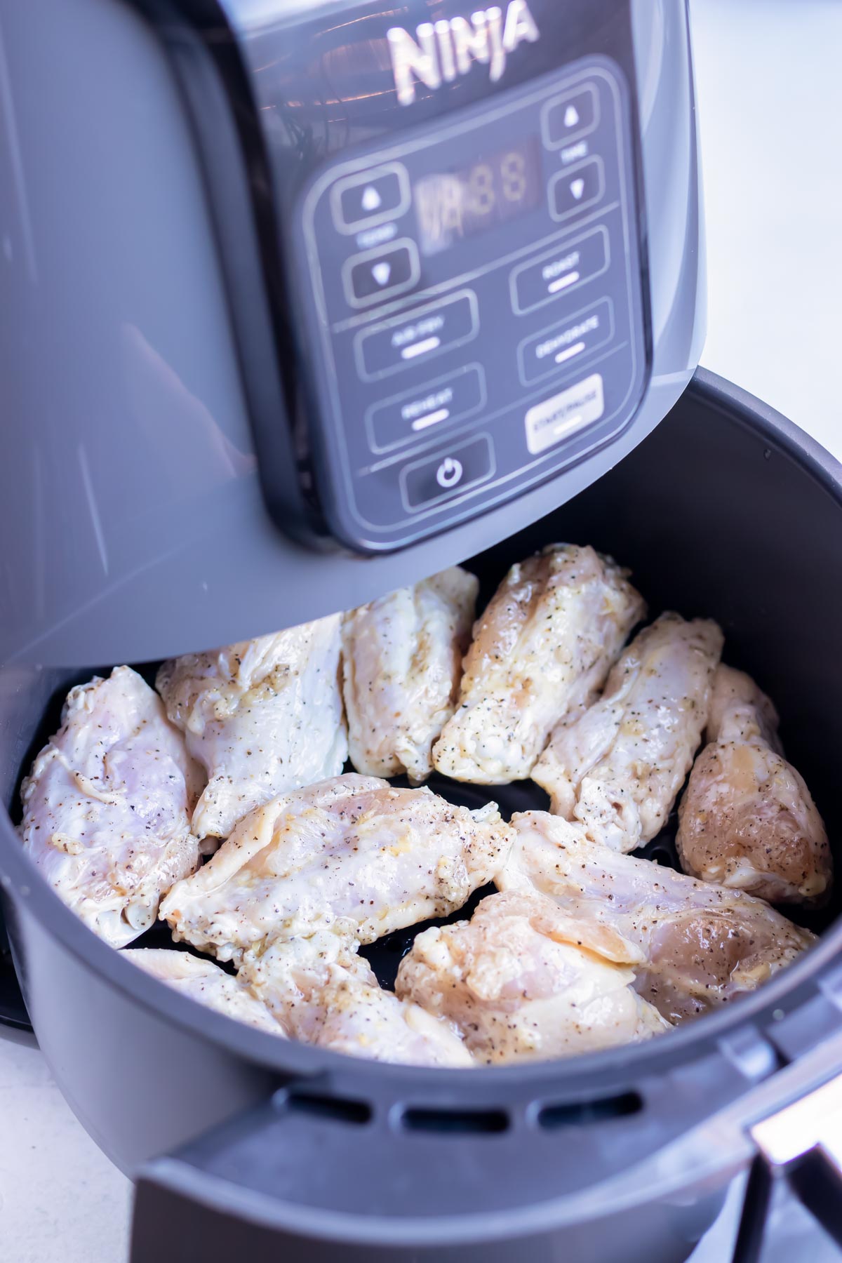 Raw chicken wings are placed in a single layer in the air fryer basket.