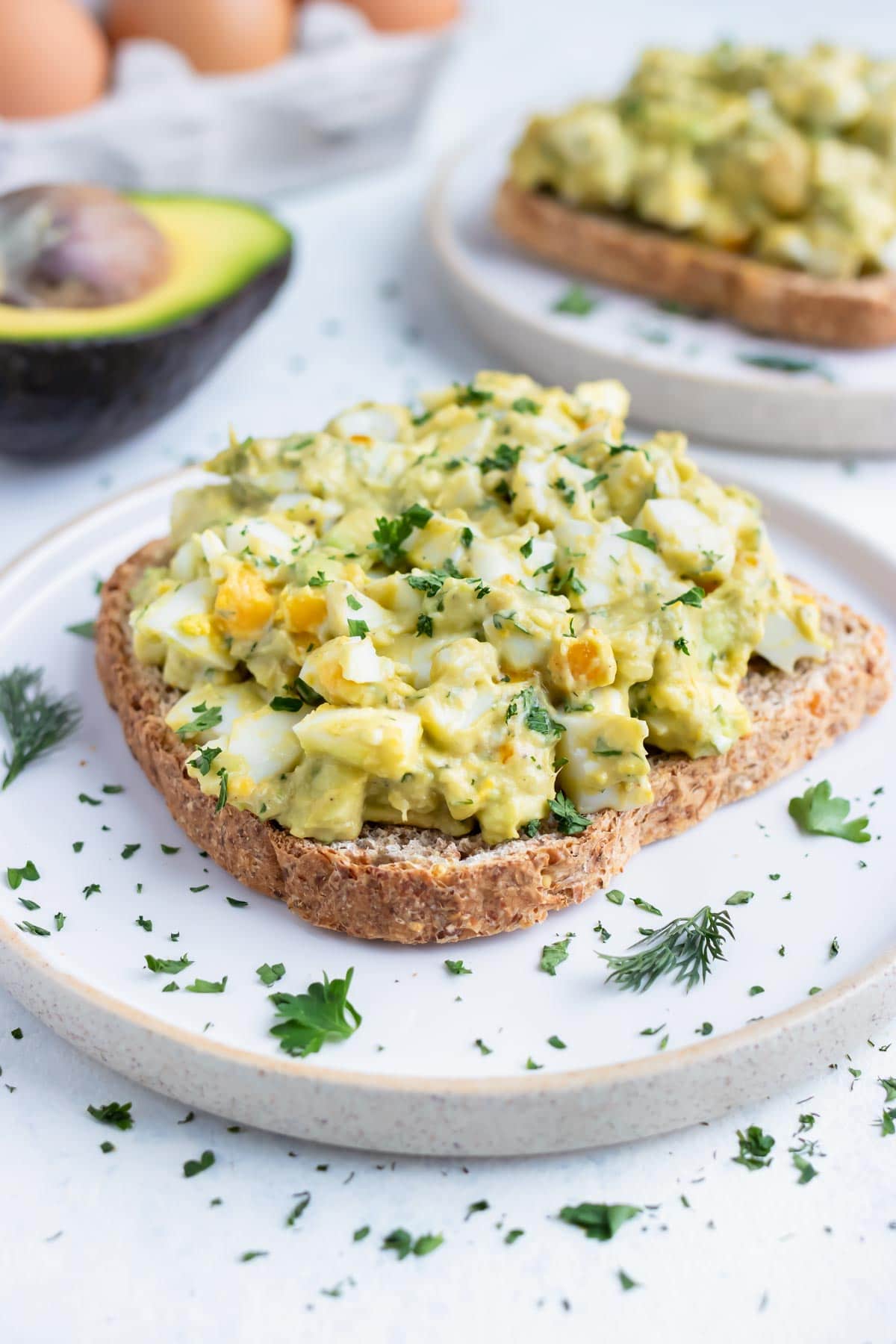 Avocado egg salad sandwiches are served on white plates.
