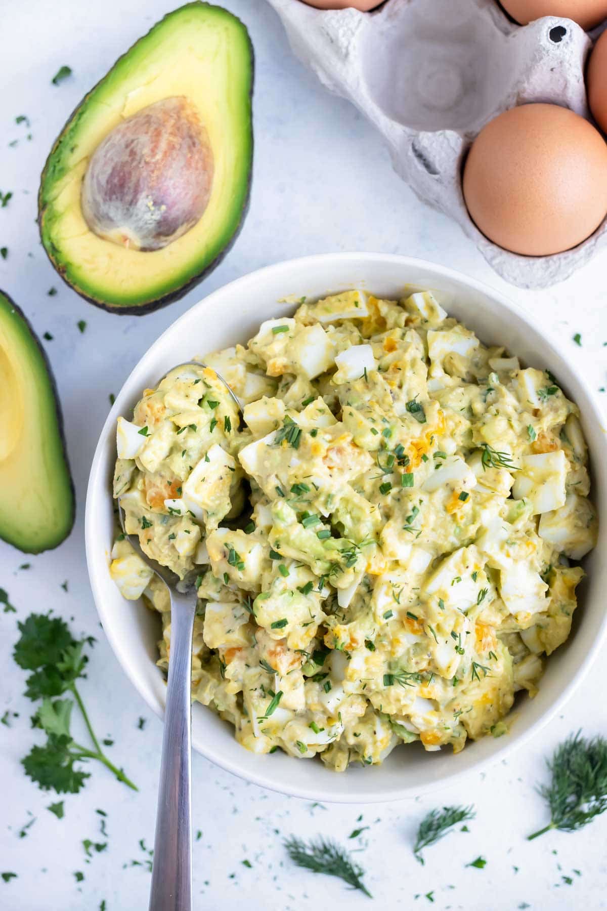 A bowl full of avocado egg salad is served with a spoon.