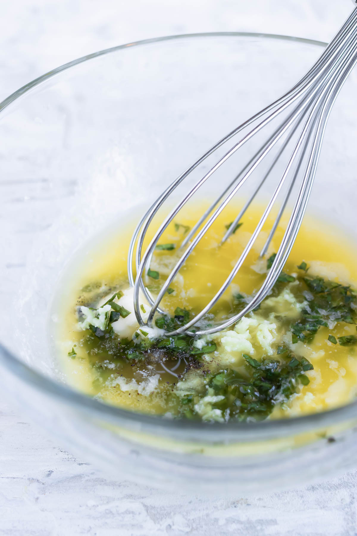 Lemon, garlic, and basil sauce being whisked in a bowl.