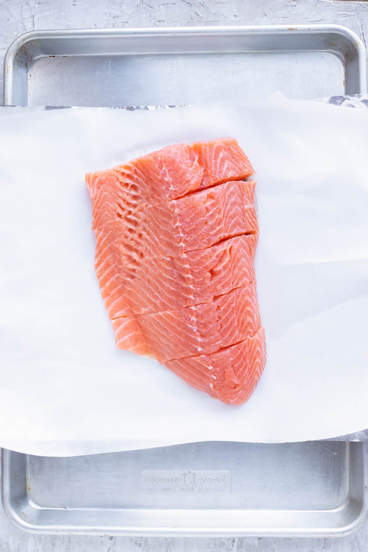 Five salmon fillets on a piece of parchment paper and foil on a baking sheet.