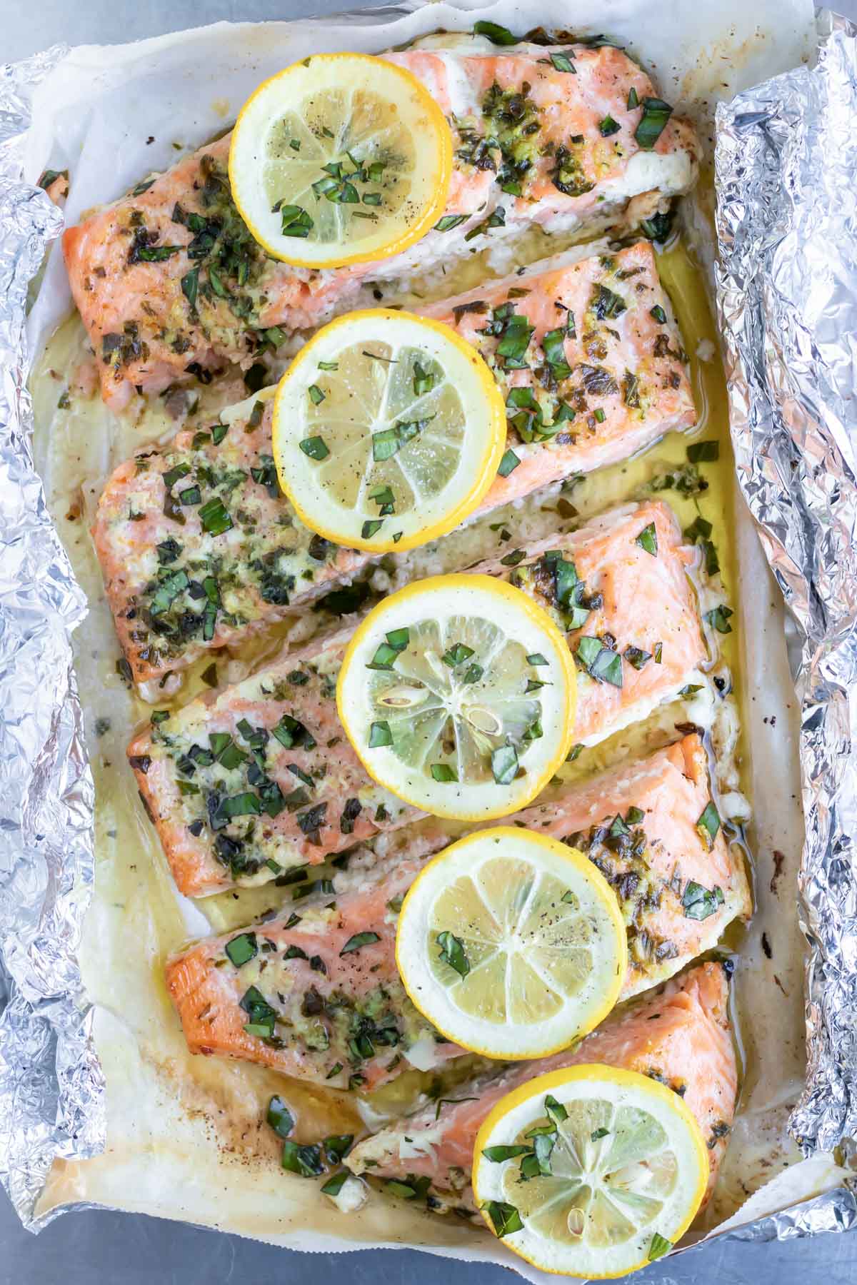 A baked salmon in a foil packet with lemon slices and fresh basil is on a baking sheet.