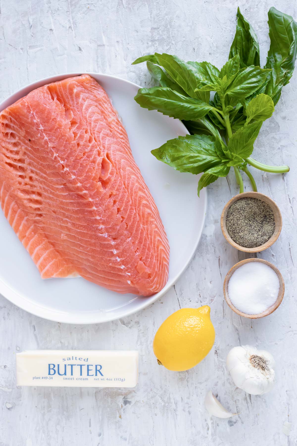 A pound of salmon, fresh basil, a lemon, garlic, salt, pepper, and butter - showing ingredients.