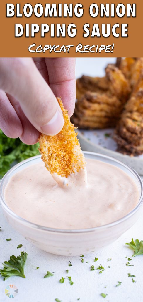 A hand is used to dip the blooming onion into the sauce.