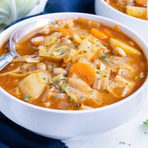 Cabbage soup is shown on the counter next to a head of cabbage.