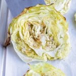 Roasted cabbage steak are lifted off a sheet pan by a spatula.
