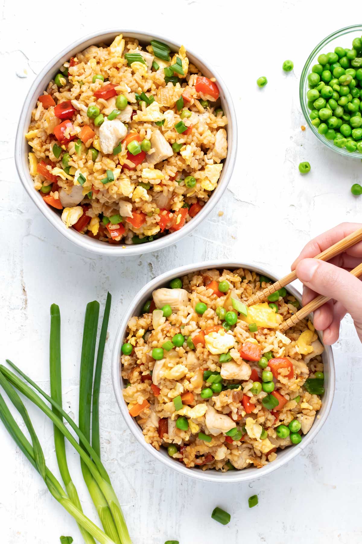 Chicken fried rice recipe being picked up with chopsticks out of a white bowl.