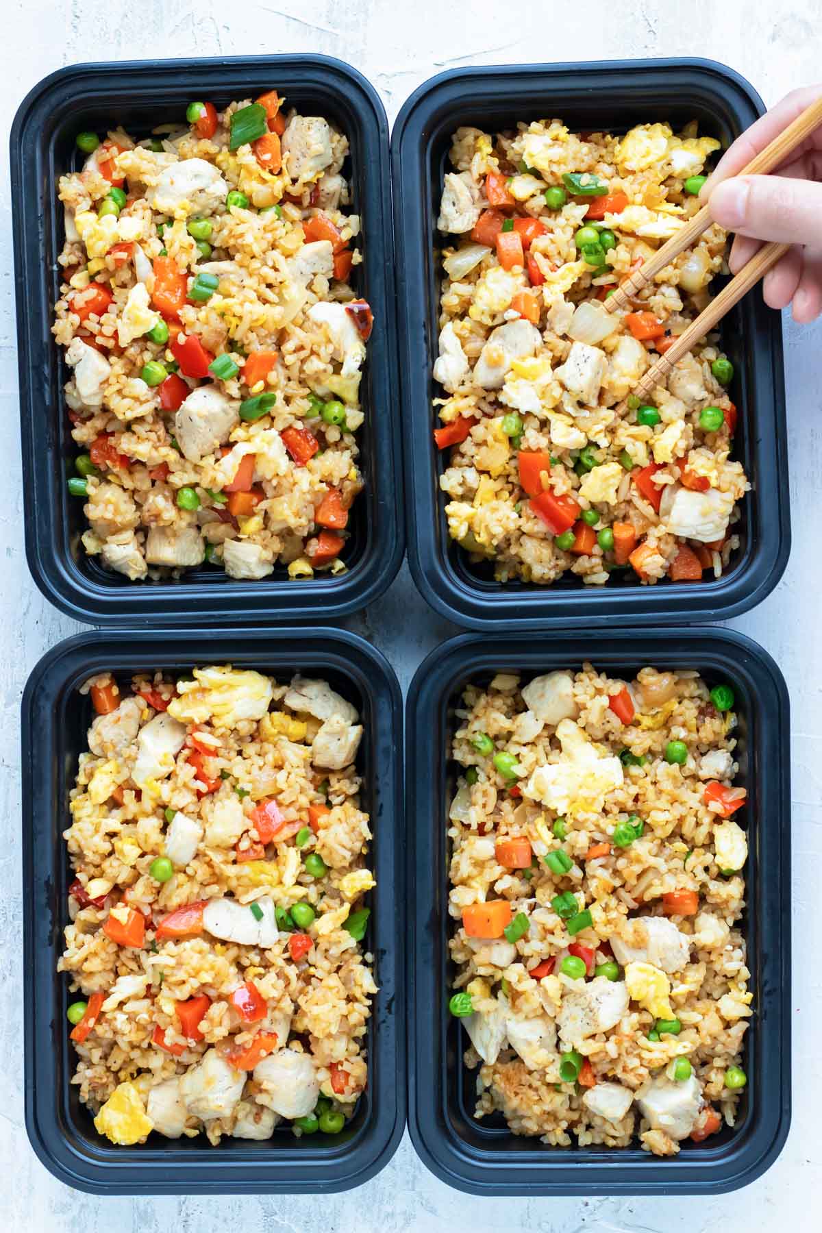 Meal prep containers full of chicken fried rice and a hand picking up some with chopsticks.