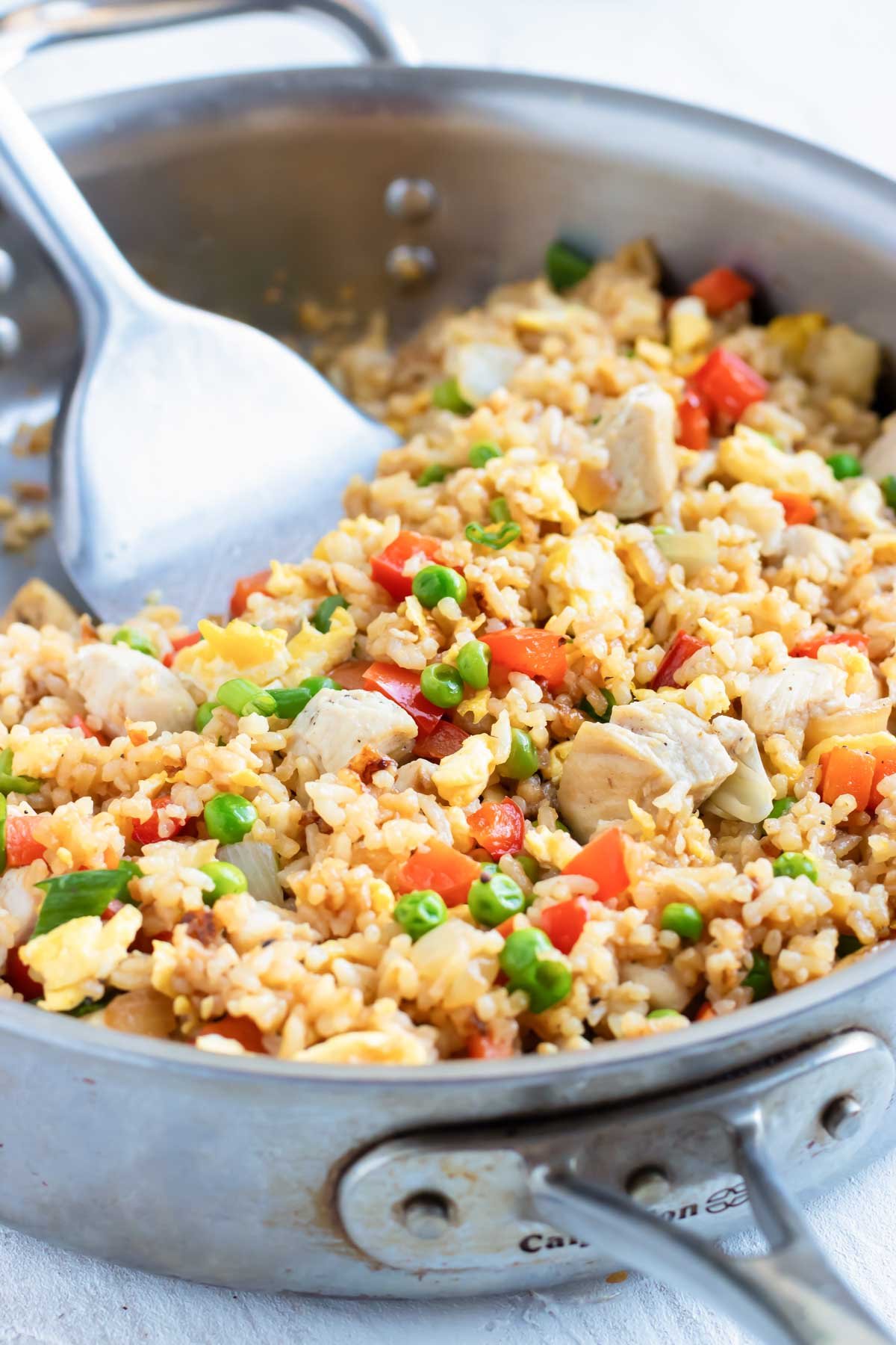 Chicken fried rice in a stainless steel skillet with a metal spatula.