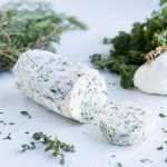 Keto friendly herb butter is shown on the counter next to garlic and herbs.