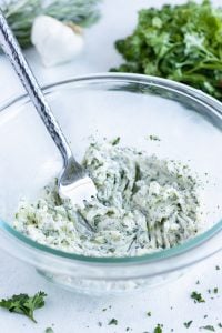 A fork is used to combine garlic herb butter ingredients together in a bowl.