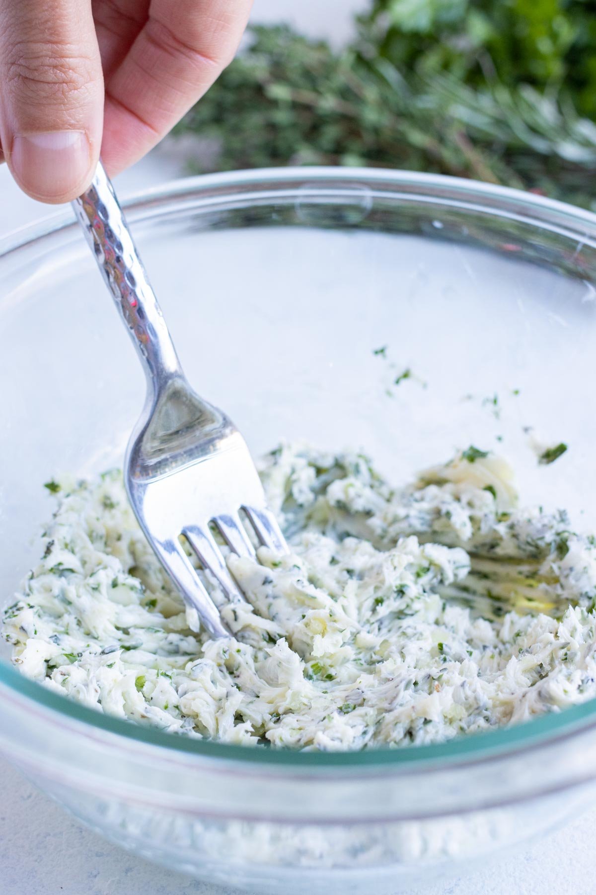 Butter and herbs are mixed together in a bowl until smooth.