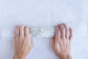 Garlic herb butter is rolled into a log using the parchment paper.
