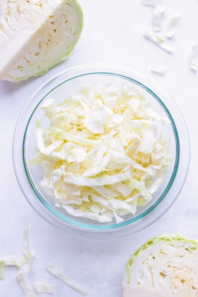 A bowl of shredded green cabbage beside a green cabbage wedge.