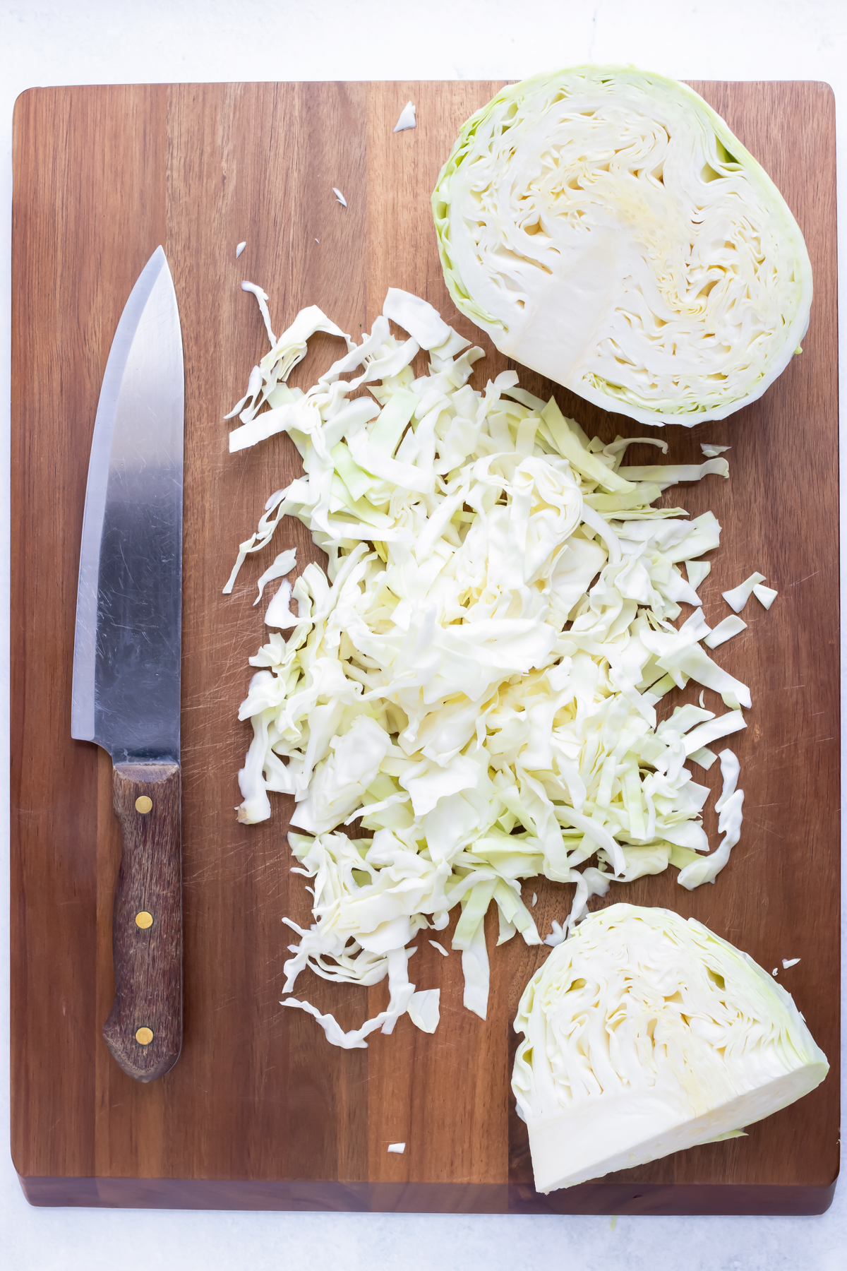 Fully shredded cabbage on a cutting board beside a knife.
