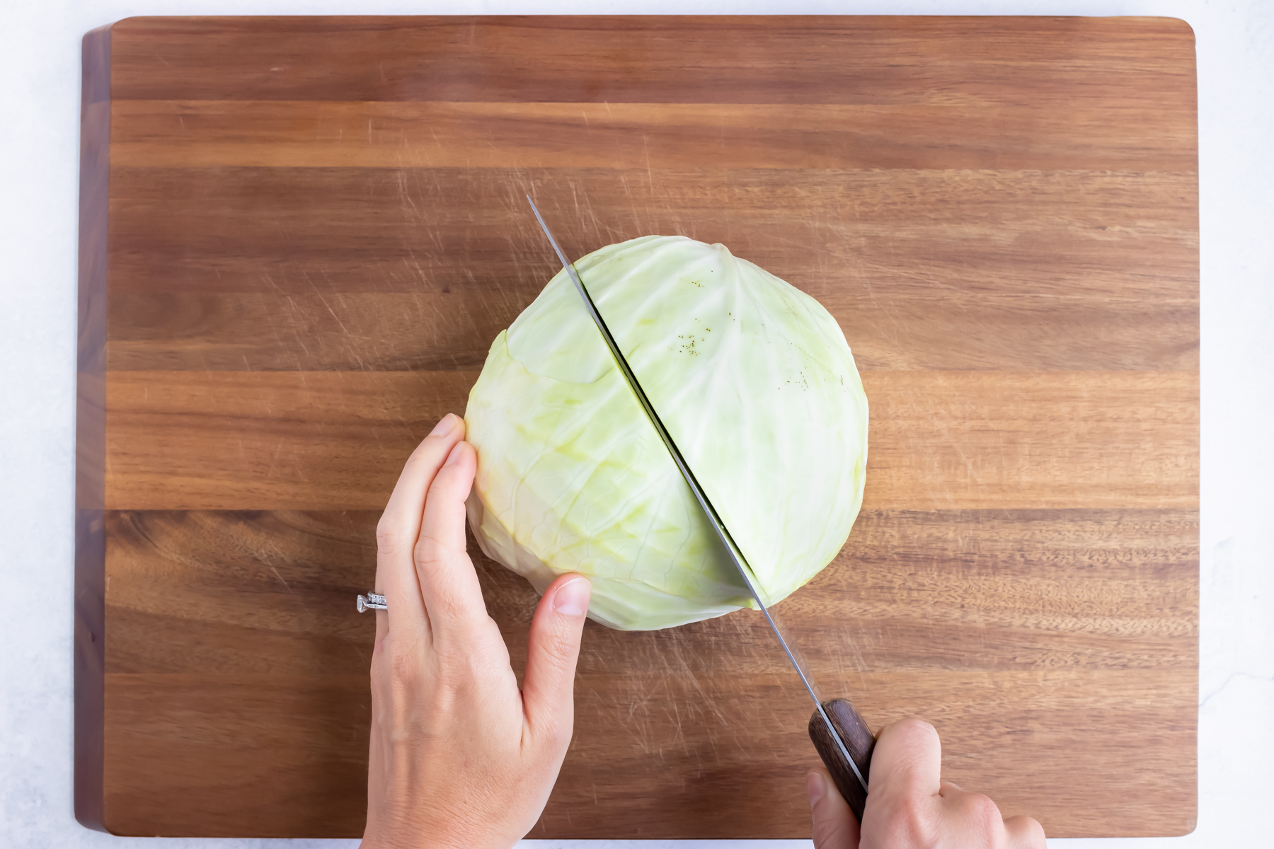 A head of cabbage with the stem side down on a cutting board being cut in half lengthwise.