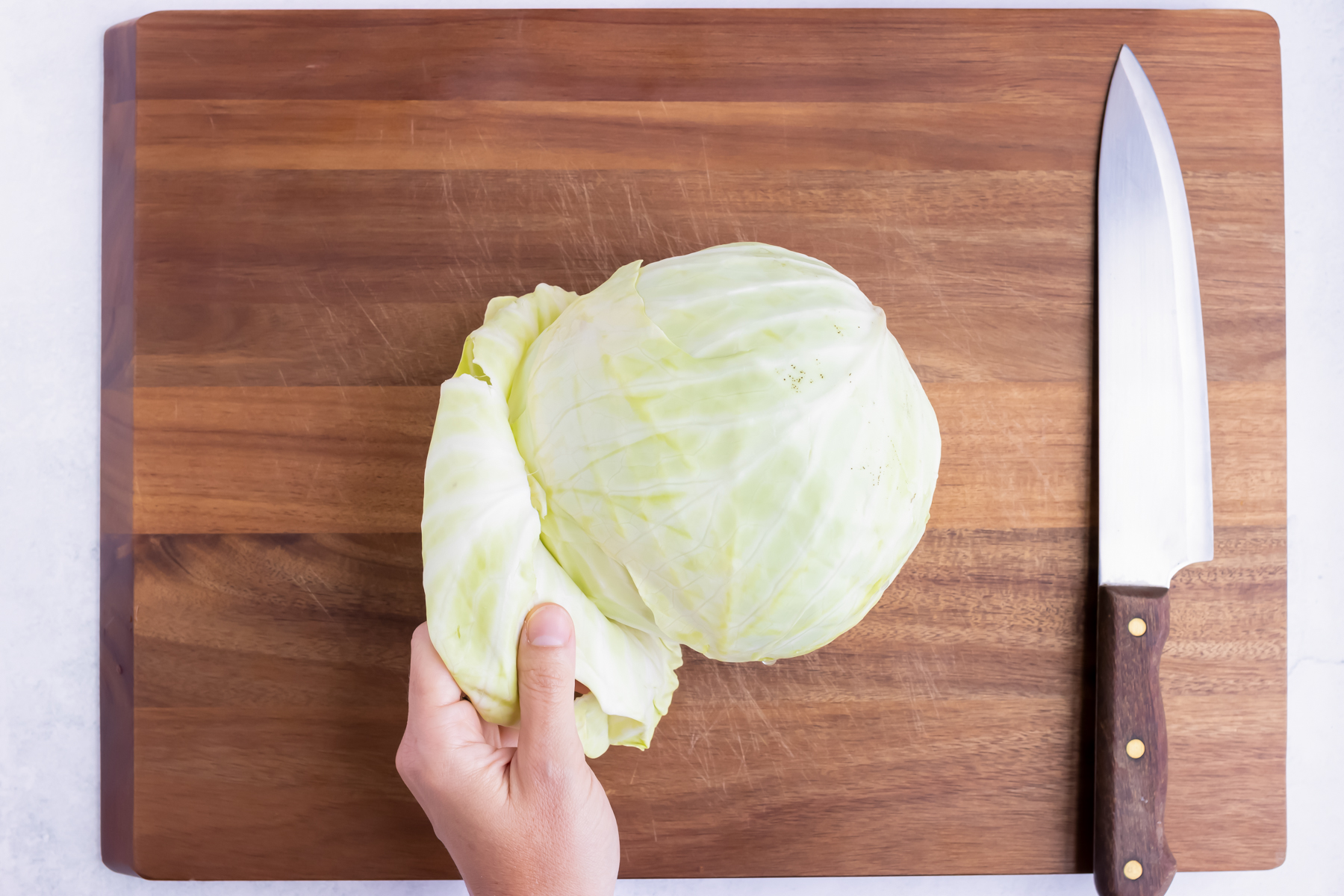 A hand pulling the outer leaves from a cabbage.