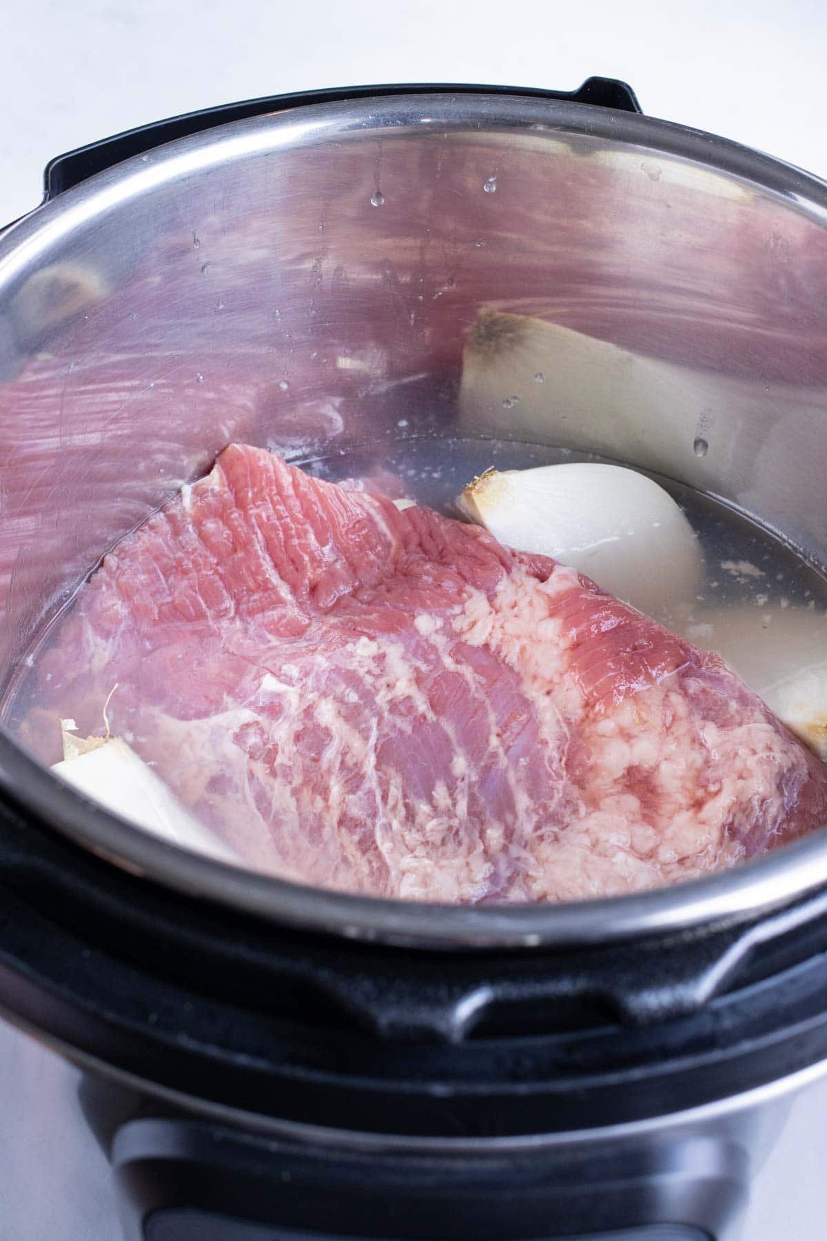 The corned beef brisket and onions are placed into the instant pot.