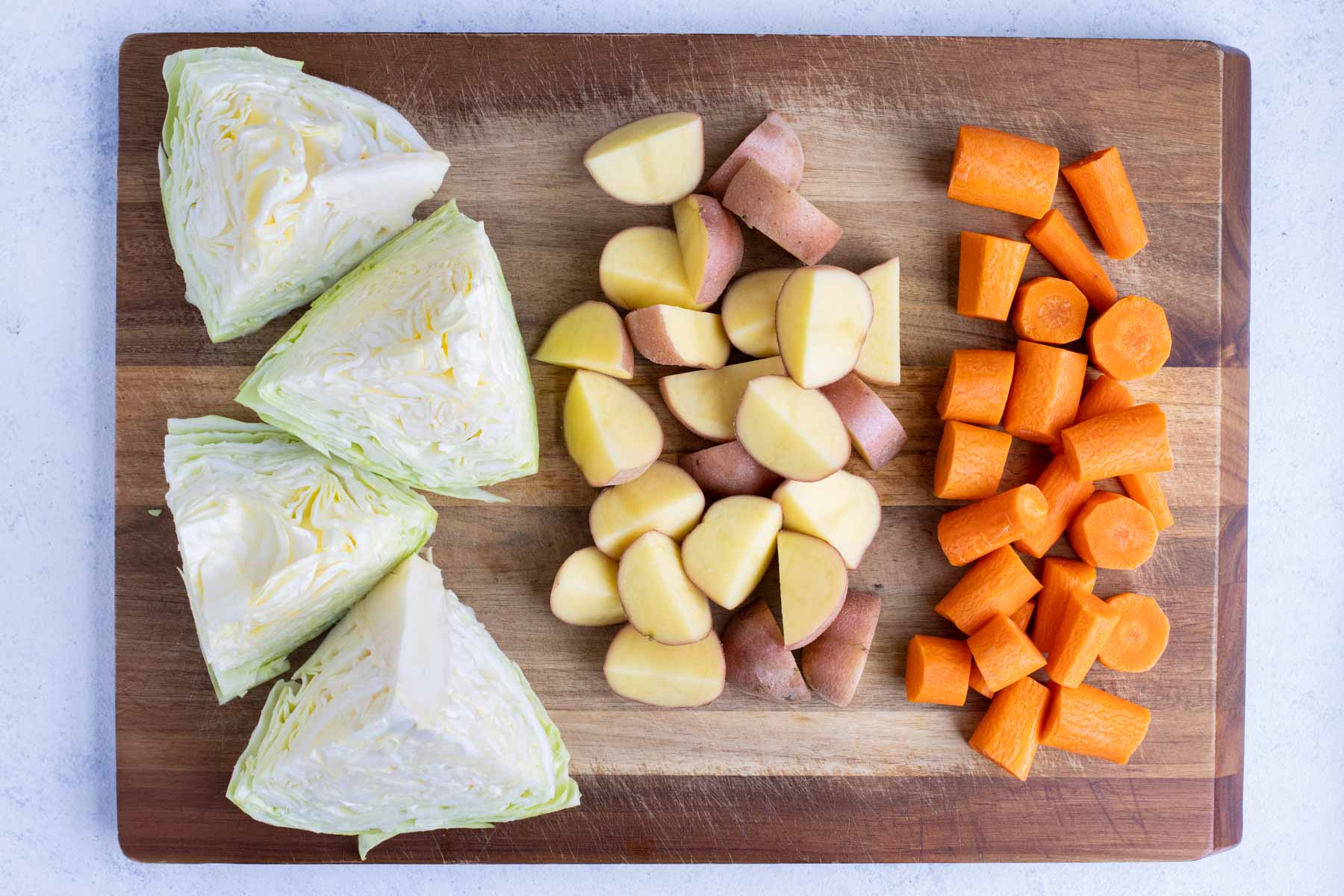 Potatoes, carrots, and cabbage are cubed on a cutting board.