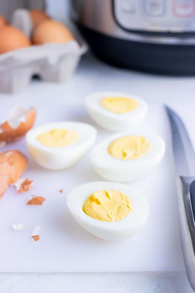 Peeled hard-boiled eggs cut in half on a cutting board for creamy potato salad.