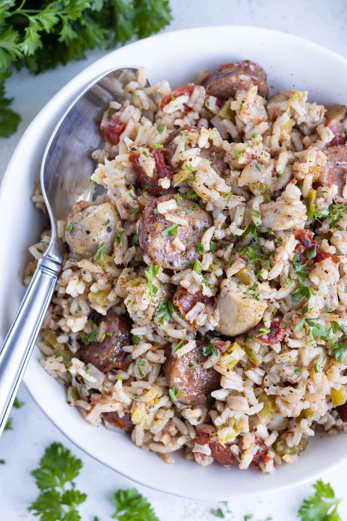 A bowl of traditional Instant Pot Jambalaya is served in a white bowl with a spoon.