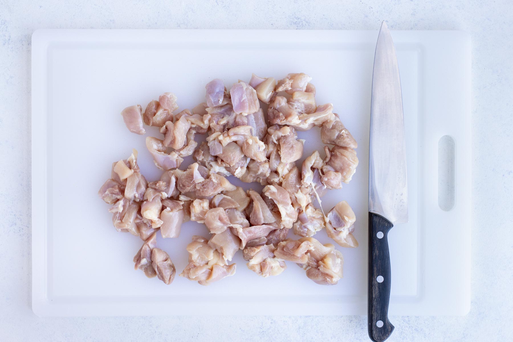 Chicken thighs are chopped into pieces with a knife.
