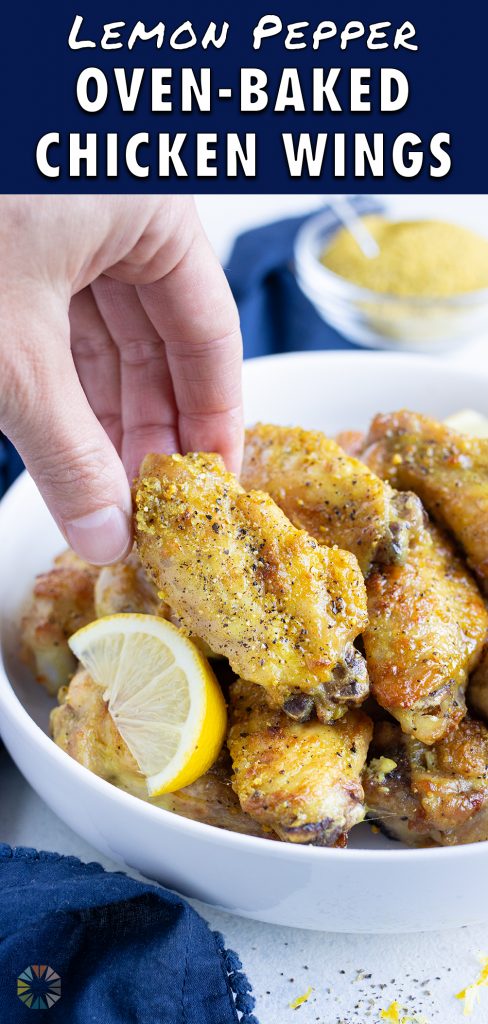 A hand is shown picking up a lemon pepper chicken wing from a bowl.