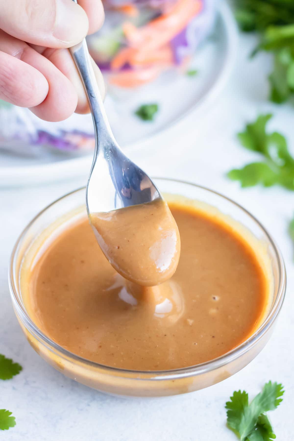 Peanut dipping sauce is dished with a spoon from a glass bowl.
