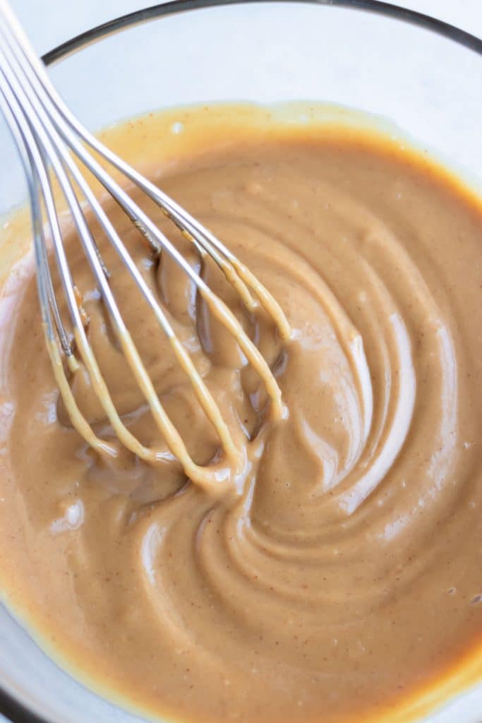 Thai peanut sauce is mixed with a whisk in a bowl.