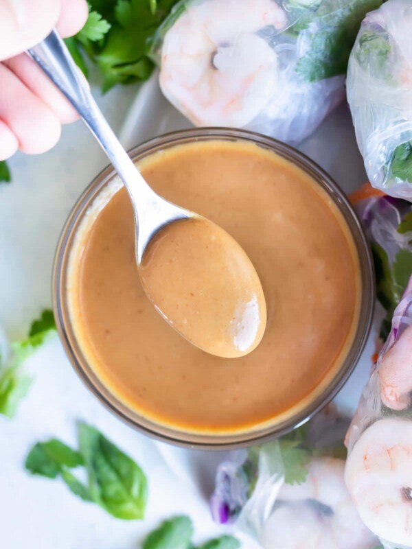 Thai peanut sauce is served with a spoon with fresh spring rolls.