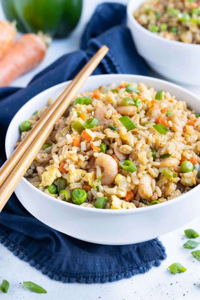 Chopsticks are shown with a bowl filled with easy shrimp fried rice.