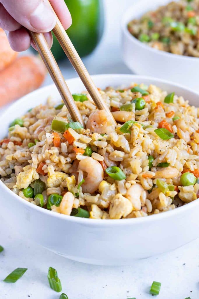 A piece of shrimp is picked up with chopsticks from a bowl of fried rice.