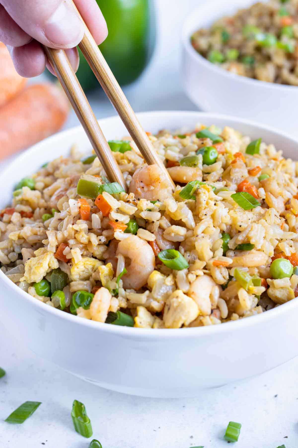 A piece of shrimp is picked up with chopsticks from a bowl of fried rice.