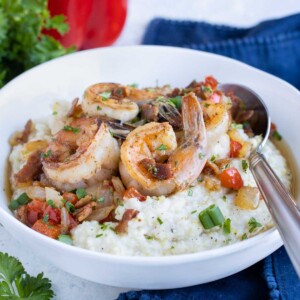 A spoon is shown with a big bowl of shrimp and grits.
