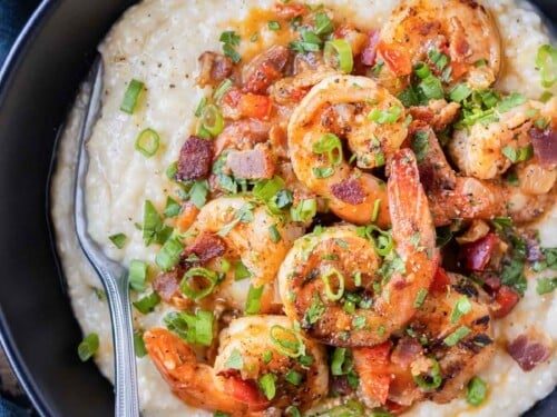 New Orleans Shrimp and Grits is served in a black bowl with green onions and parsley on top.