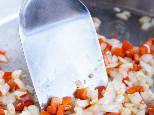 Diced onions and bell peppers are cooked in a pan.